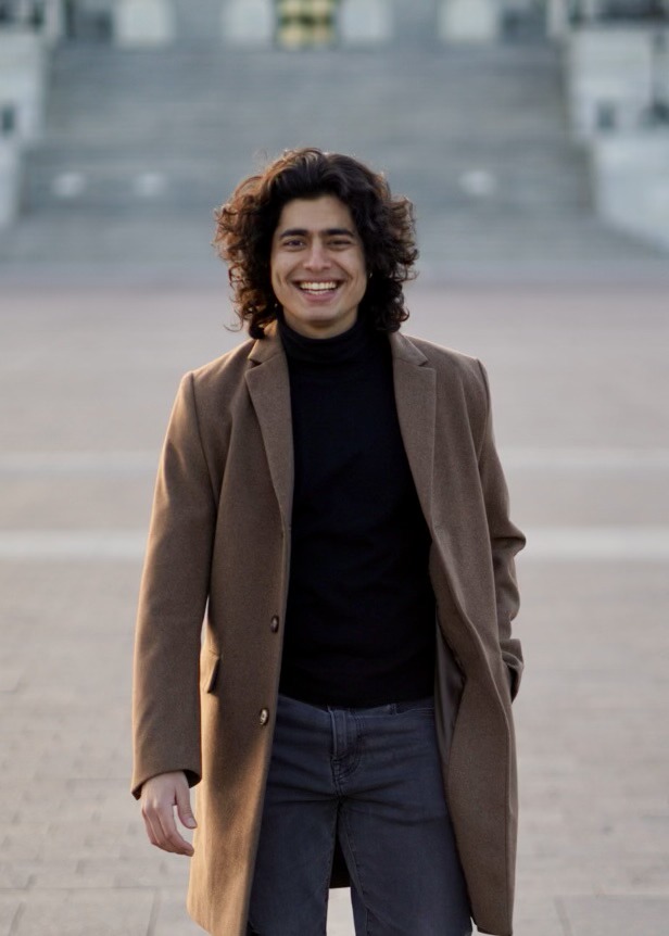 Anmol Arora smiling outdoors and wearing a brown coat